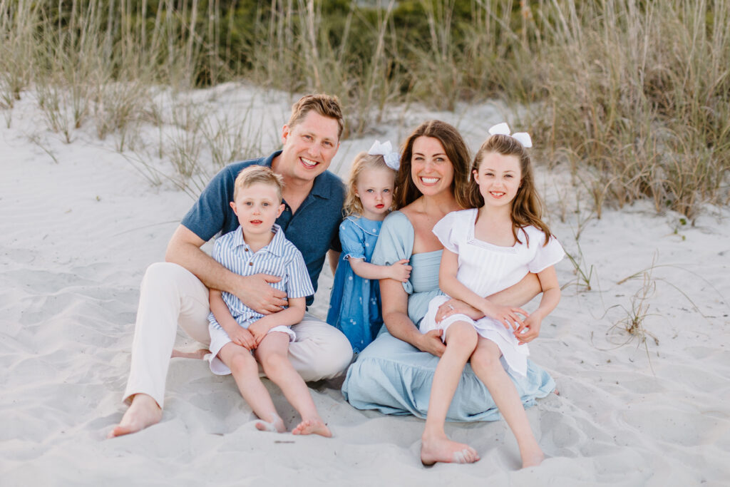 Smiling family sitting on the beach in Hilton Head, dressed in festive summer outfits, capturing memories ahead of the 4th of July fireworks in Hilton Head and the Lowcountry.