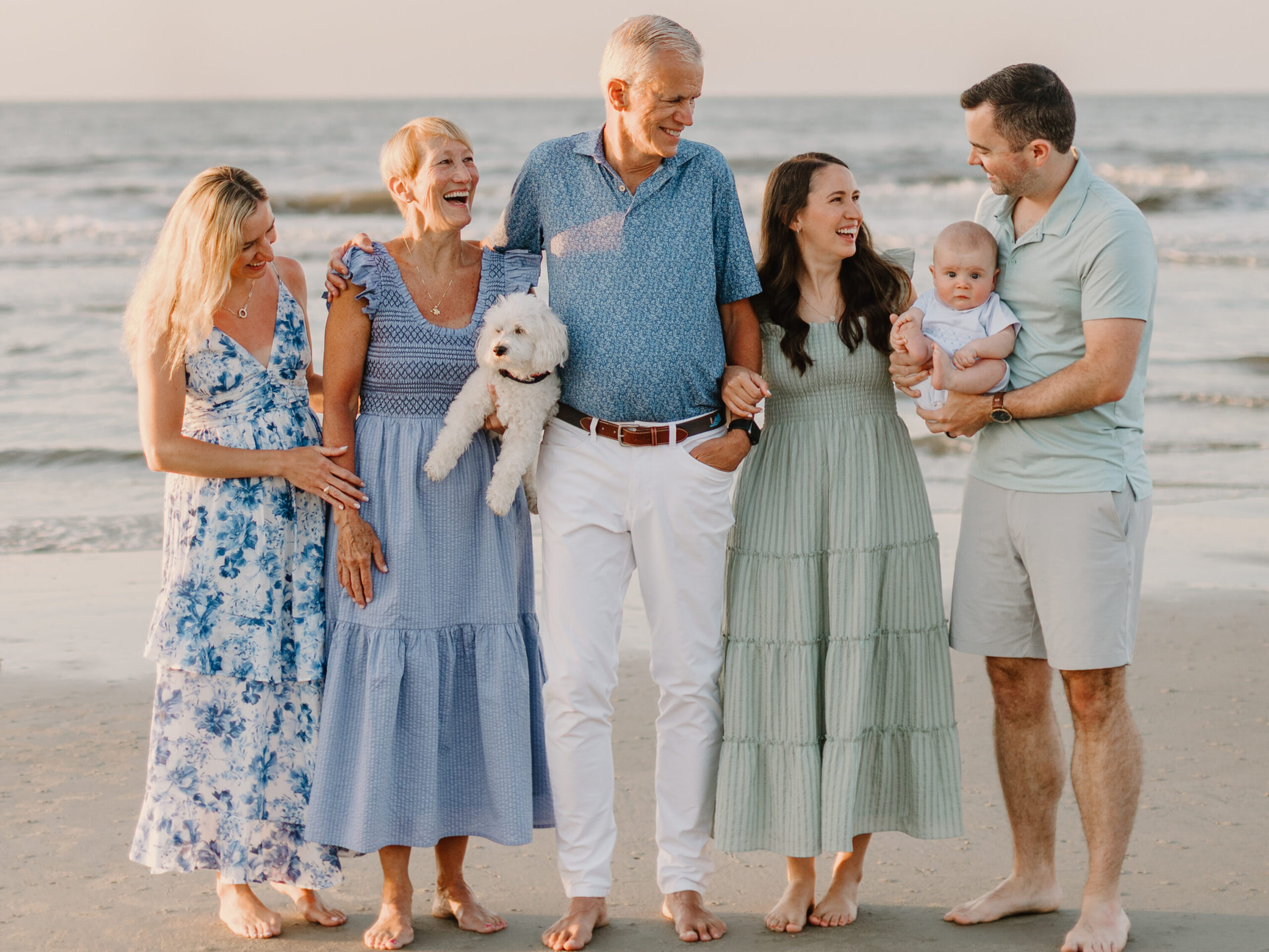 Smiling family of four with their dog posing together on a sandy Hilton Head Island beach at sunset, surrounded by soft waves and warm golden light.